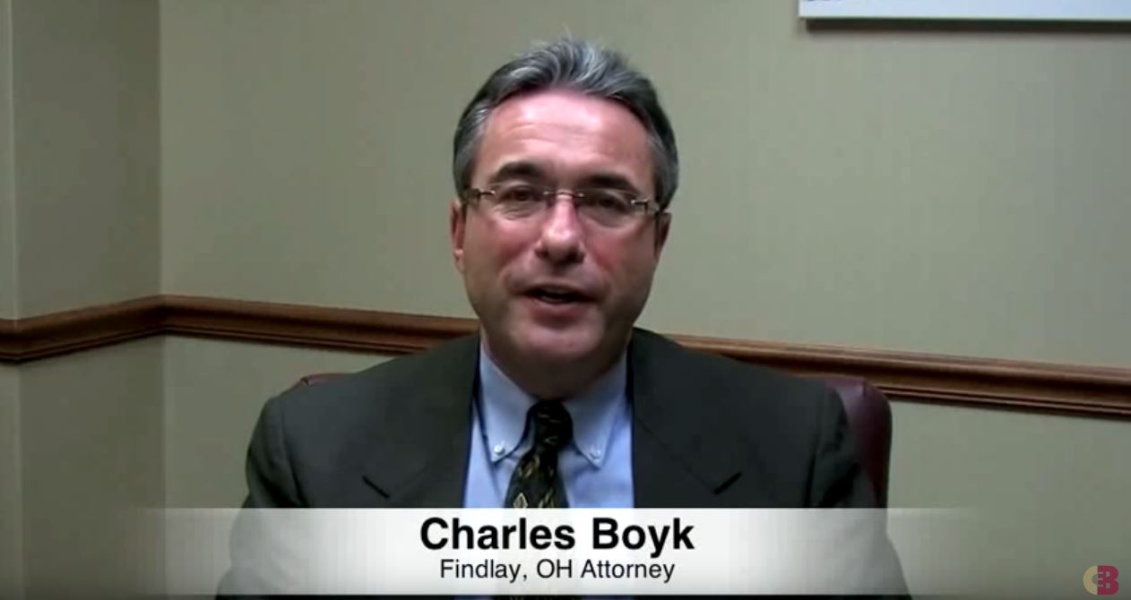 Charles BOyk sitting and speaking and a footer with his name