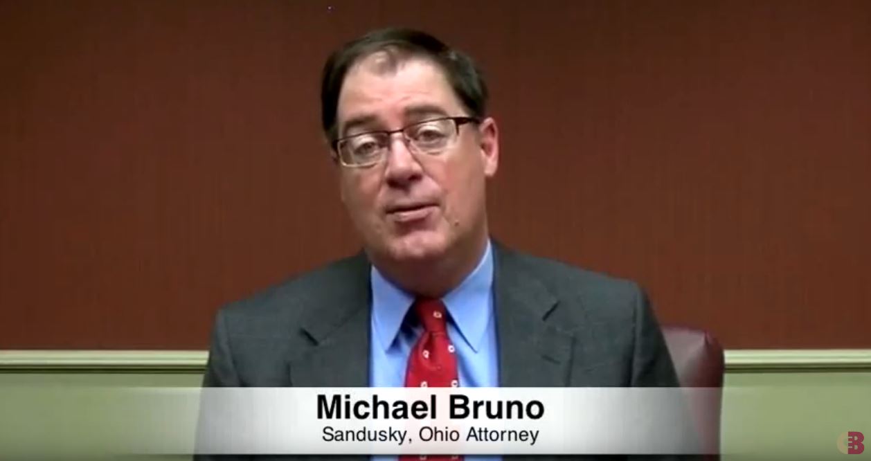 Michael Bruno sitting and speaking, and a text at bottom with his name