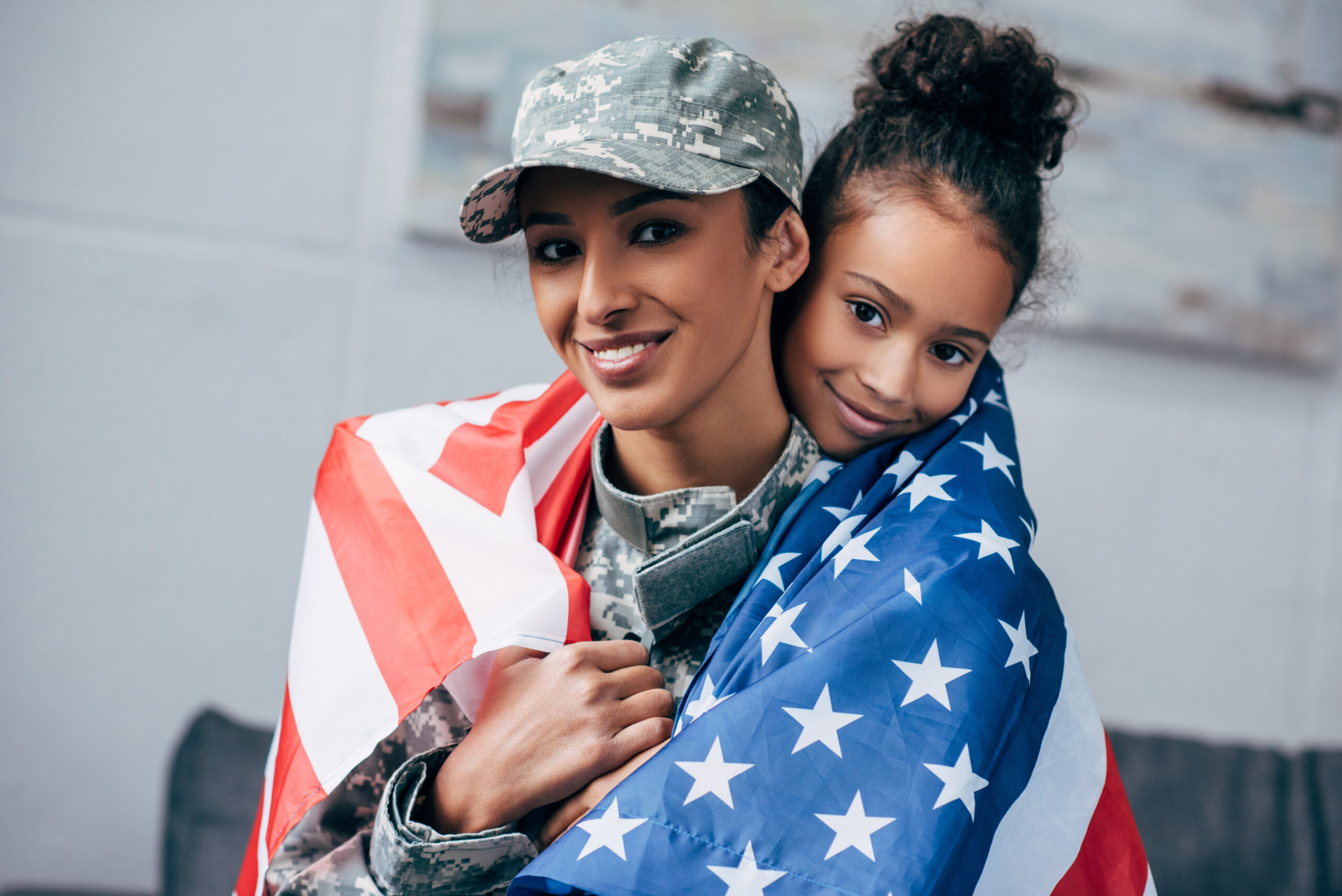 african american daughter and female soldier in military uniform wrapped with american flag at home